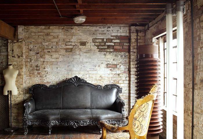 Черный диван около грубо отделанной кирпичной стены